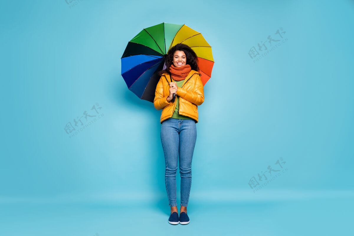 年轻美丽的黑皮肤女士站在蓝色的背景上 带着五颜六色的伞多民族非洲牛仔裤
