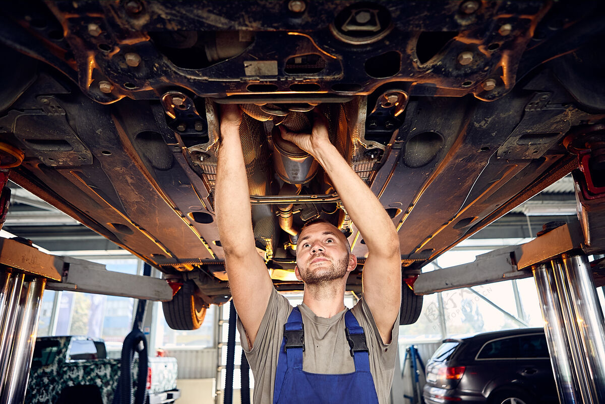 机械帅气的汽车修理工在加油站检查汽车的传动装置诊断修理工作