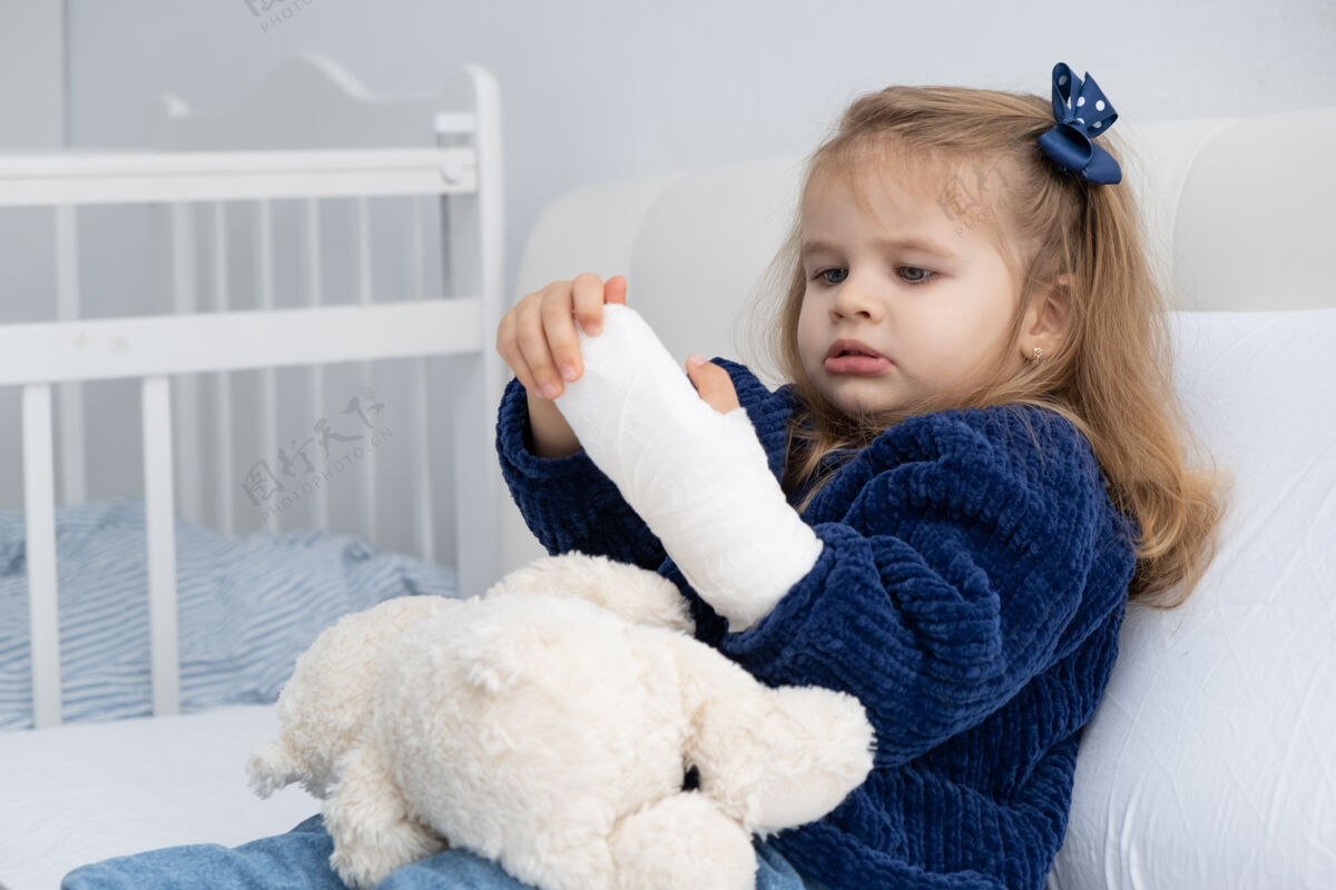 矫形一个金发碧眼的小女孩手拿石膏坐在床上伤害童年手