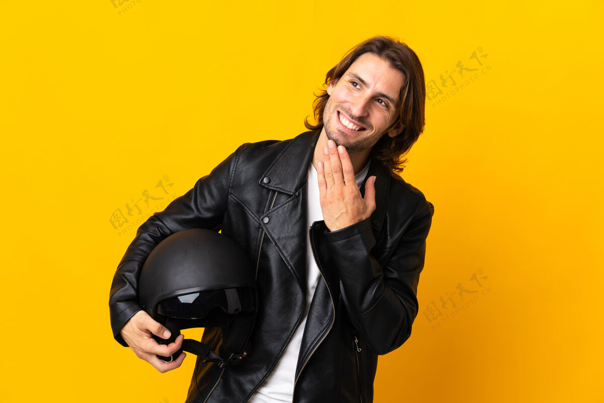 头一个戴着摩托车头盔的男人站在黄色的墙上微笑着抬头看摩托车手摩托车手幸运