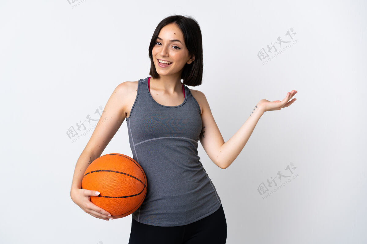 人打篮球的年轻女子孤零零地站在白色的墙上 向旁边伸出双手 欢迎前来运动装比赛酷