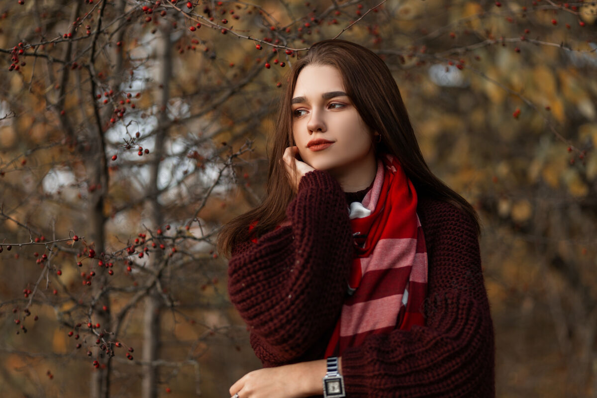 时尚穿着紫红色针织毛衣和格子围巾的年轻女子在公园里摆姿势格子毛衣围巾