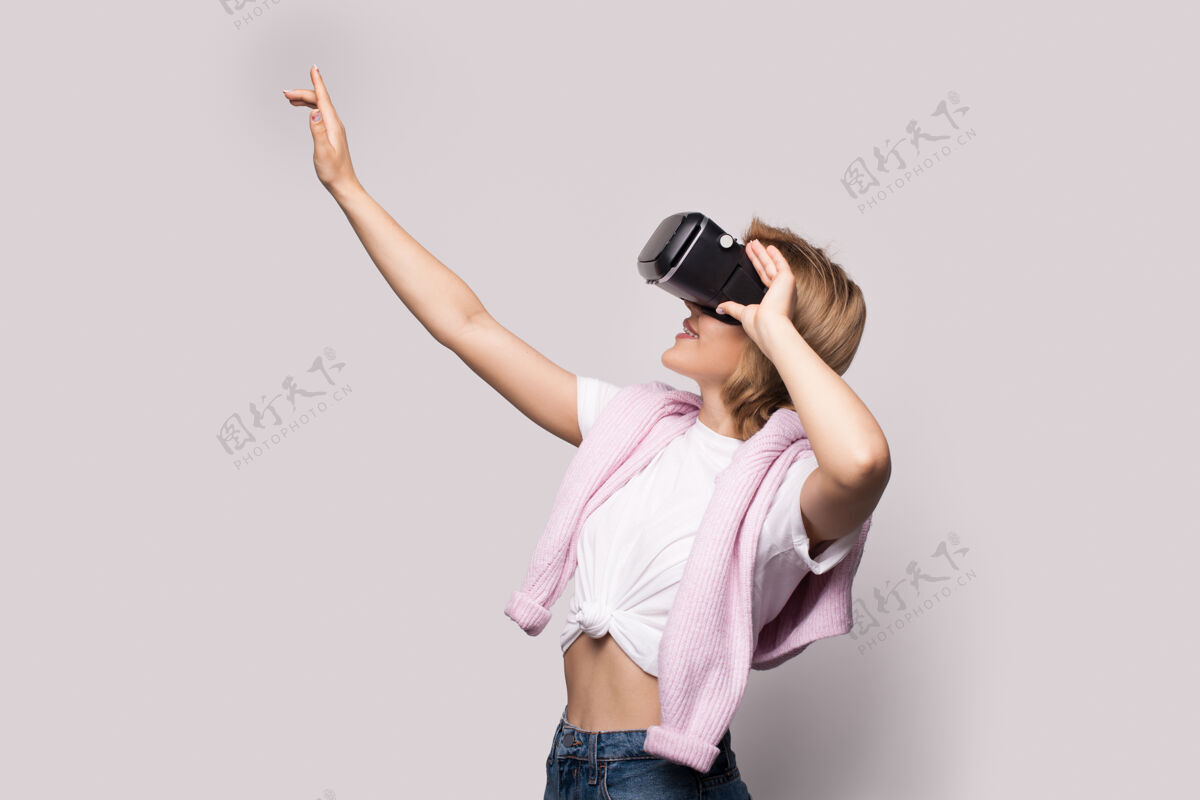 室内一位金发白种女人在一个虚拟现实体验中用一个白色工作室墙上的特殊耳机触摸着什么东西指向未来按下