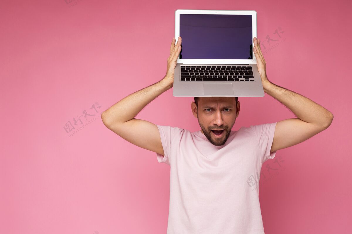 笔记本电脑一个帅哥拿着笔记本电脑 在孤立的粉色背景下 穿着t恤看着相机在线设备显示器