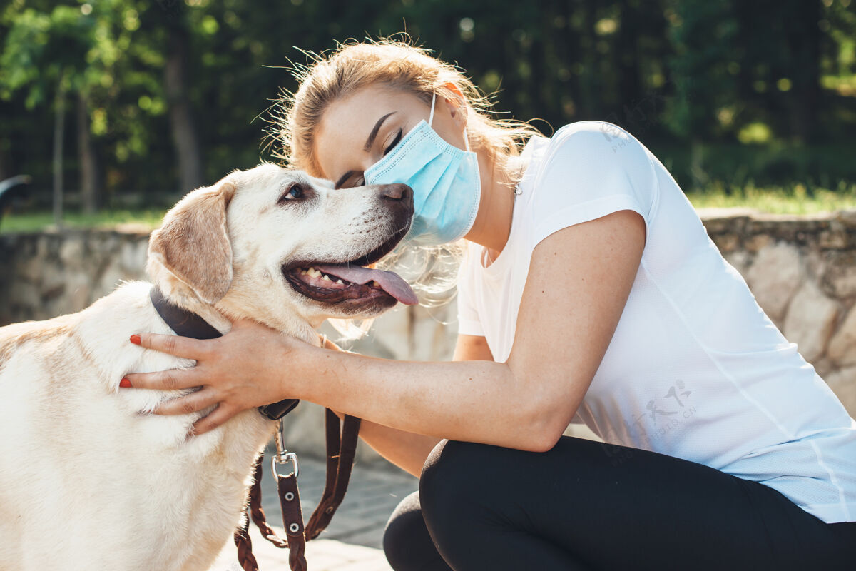 健康一位戴着医用面罩 金发的白种女人在公园散步时拥抱着她的拉布拉多犬症状封闭传染