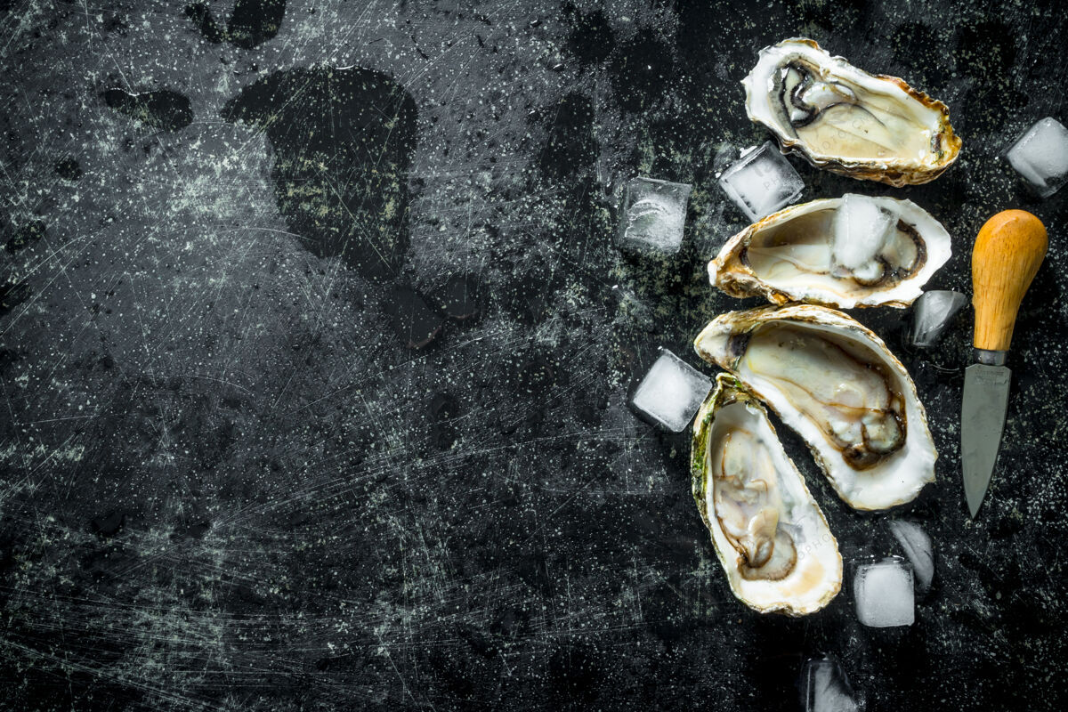 晚餐海鲜好吃在深色的木桌上放一把刀和冰牡蛎顶视图配料牡蛎