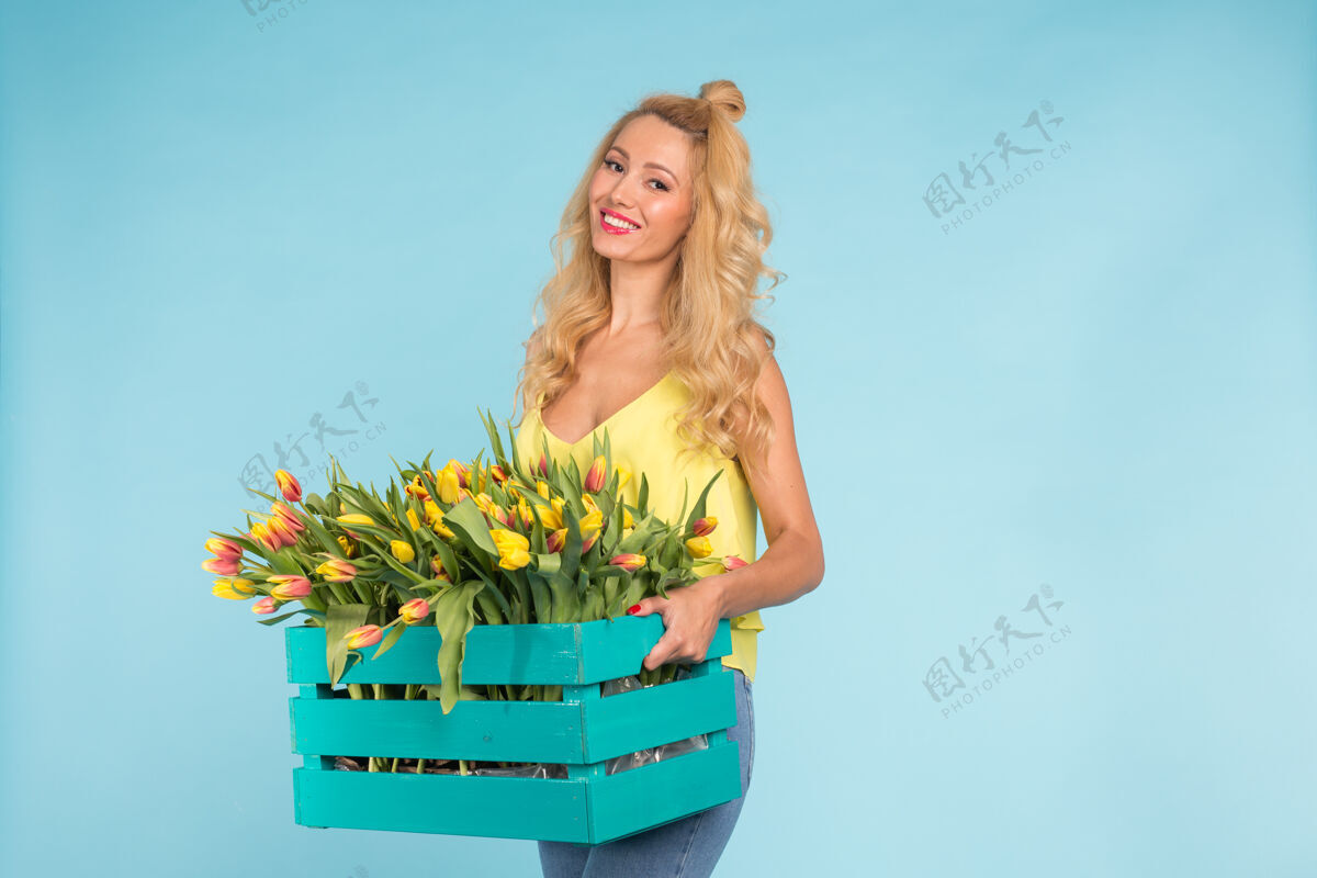 女人开朗的年轻金发女花店 蓝色墙上挂着一盒郁金香 还有复印空间花卉职业工作