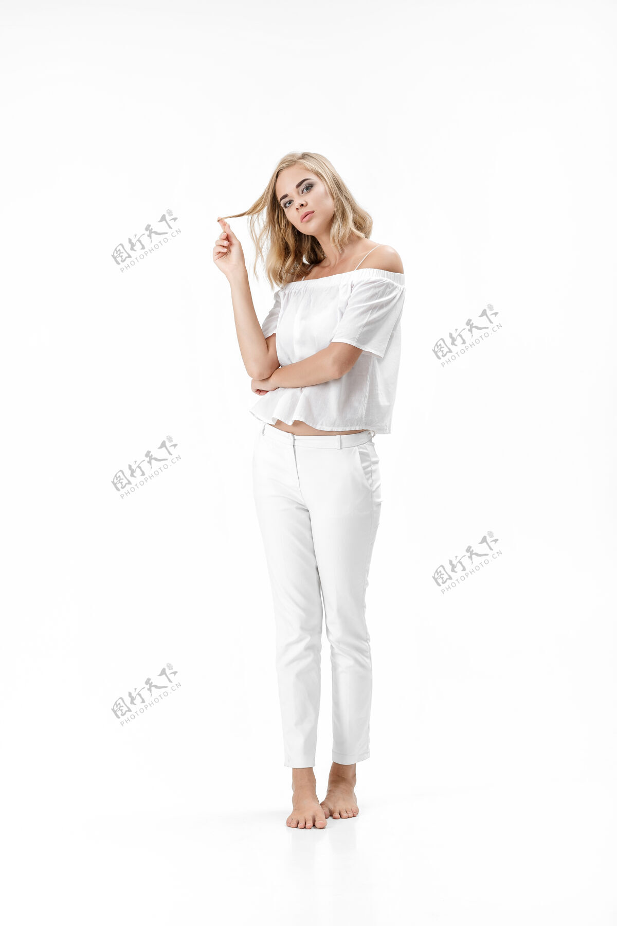 年轻美丽严肃的金发女人在白色的背景上穿着白色的衬衫和裤子模特健康衣服