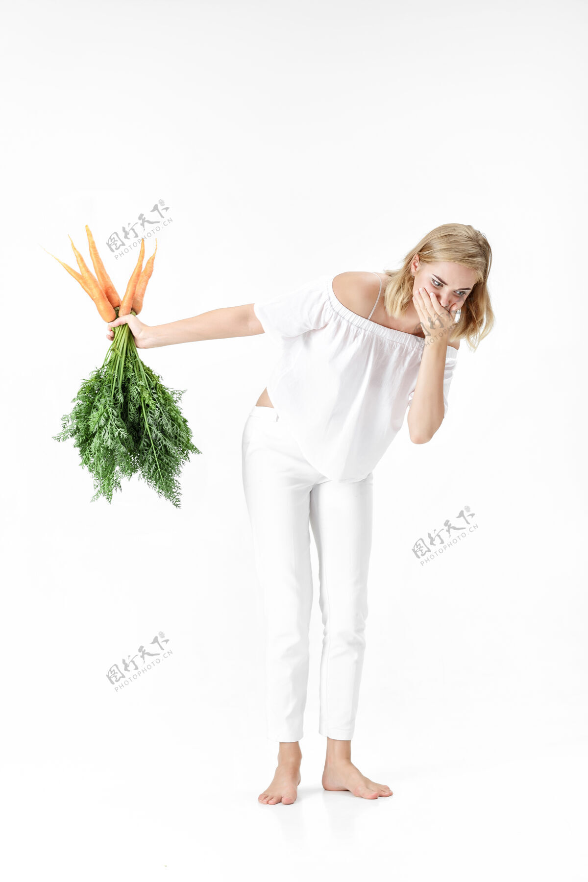 新鲜一个穿着白衬衫的金发女人 手里拿着一根白衬衫上有绿叶的胡萝卜背景女孩吃胡萝卜和节食的感觉不好美丽生欢呼