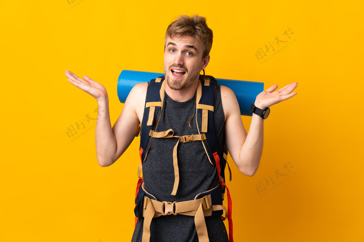 旅行背着一个大背包的年轻登山者 被隔离在黄色背景下 表情震惊成人帅哥背包