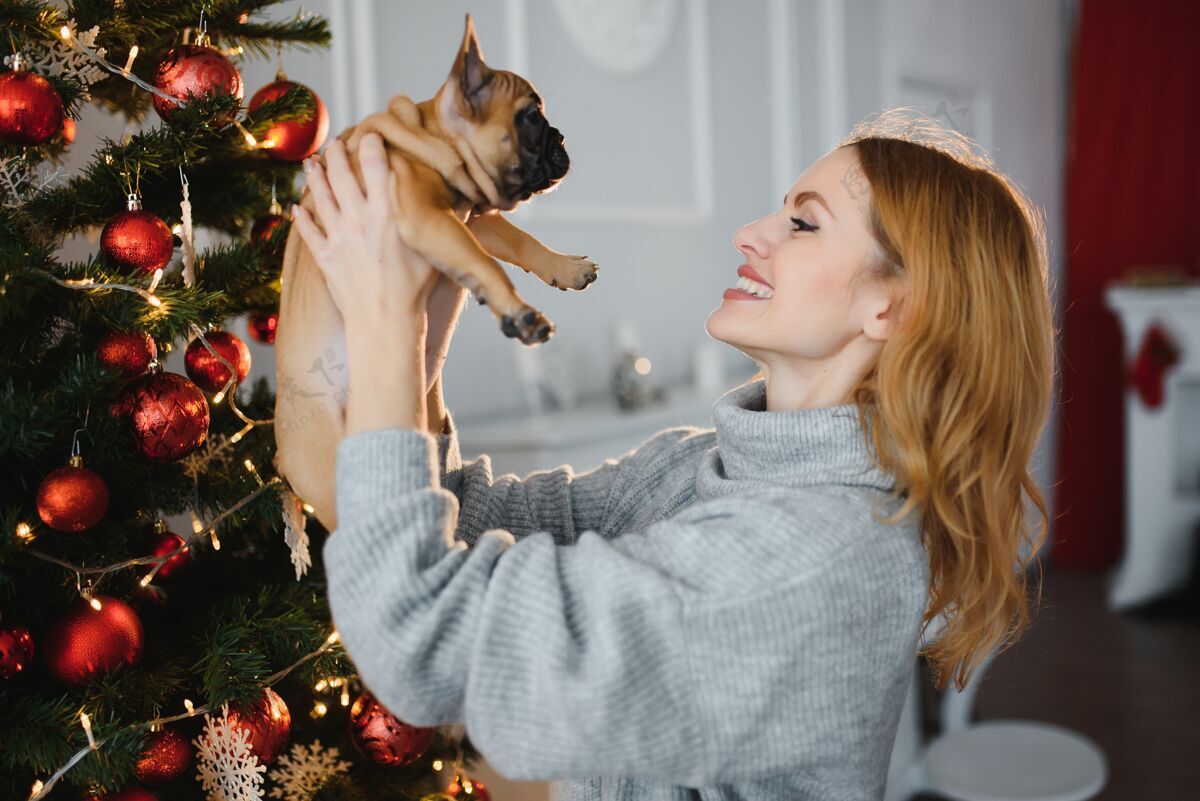 爱美丽的年轻女子带着一只小狗在圣诞庆典的背景下女孩快乐欢呼