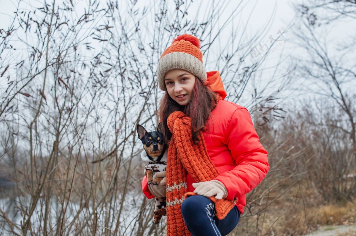 人女孩10岁老年人穿着橙色夹克 戴着帽子和帽子的女孩围巾女孩以及吉娃娃走路一只宠物自然模特人