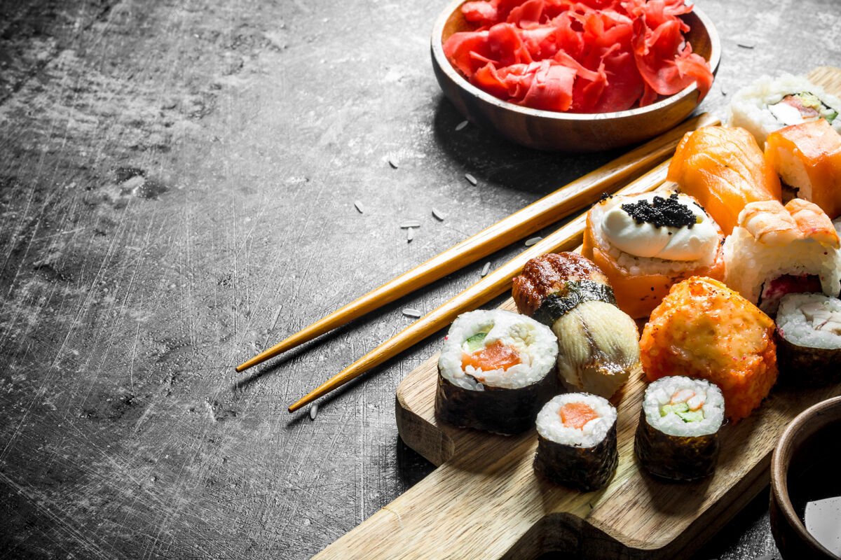 日本不同种类的寿司 麦片和卷放在切菜板上 配以生姜和大豆沙司黑暗的乡村背景酱油鲑鱼鳄梨