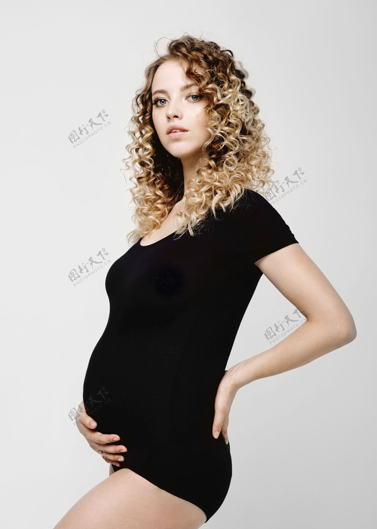 生活怀孕的年轻漂亮的时装模特儿在灰色的工作室里穿着黑色的身体肖像年轻女人
