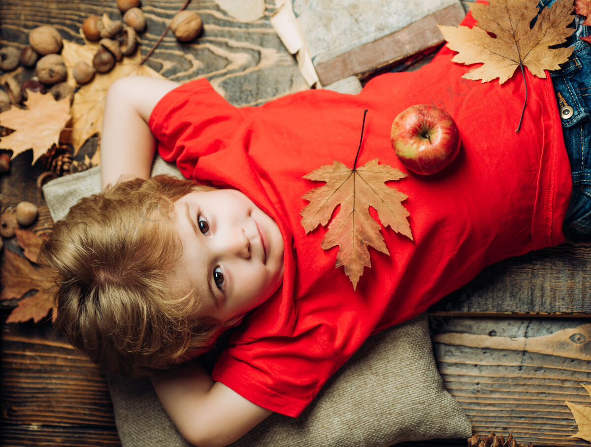 甜蜜秋天 金发男孩趴在木地板上 肚子上放着一个苹果离开所有秋季服装的最大折扣孩子们孩子们在秋天玩时间秋天玩具