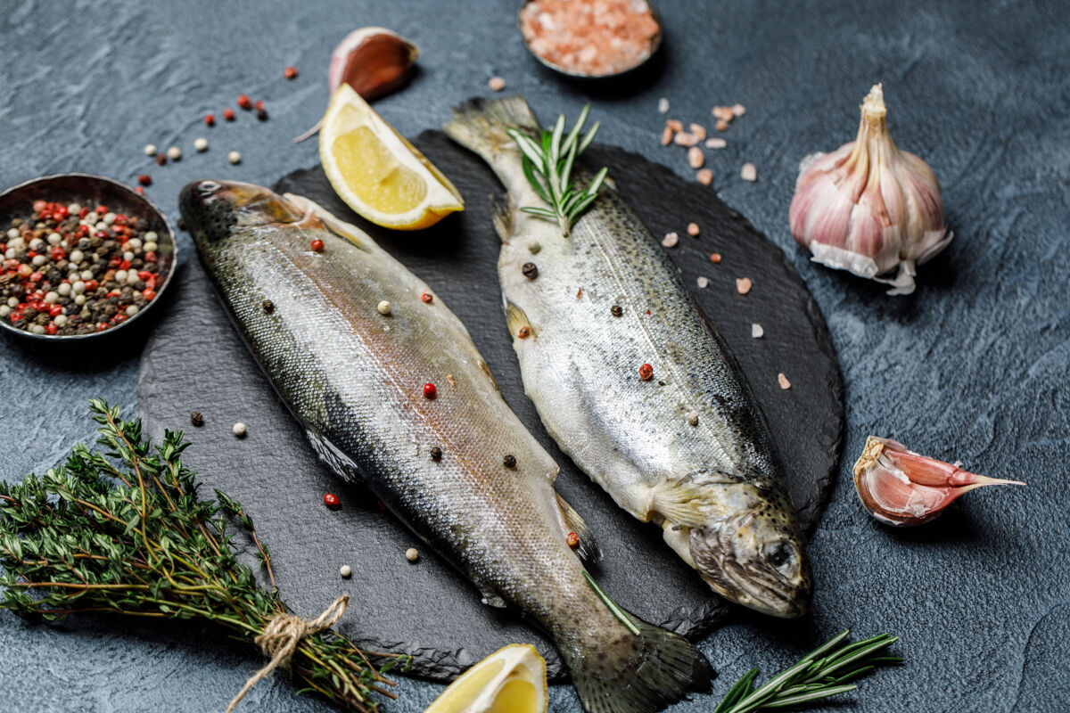 欧米茄新鲜的河鳟鱼 用香料和配料在深色石头背景上烹饪膳食健康鳟鱼