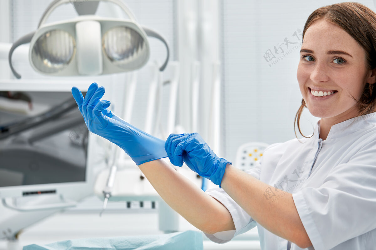 牙科一位女牙医戴上手套 在牙科办公室的牙科设备的背景下愉快的病人和牙医的概念工作手术牙科