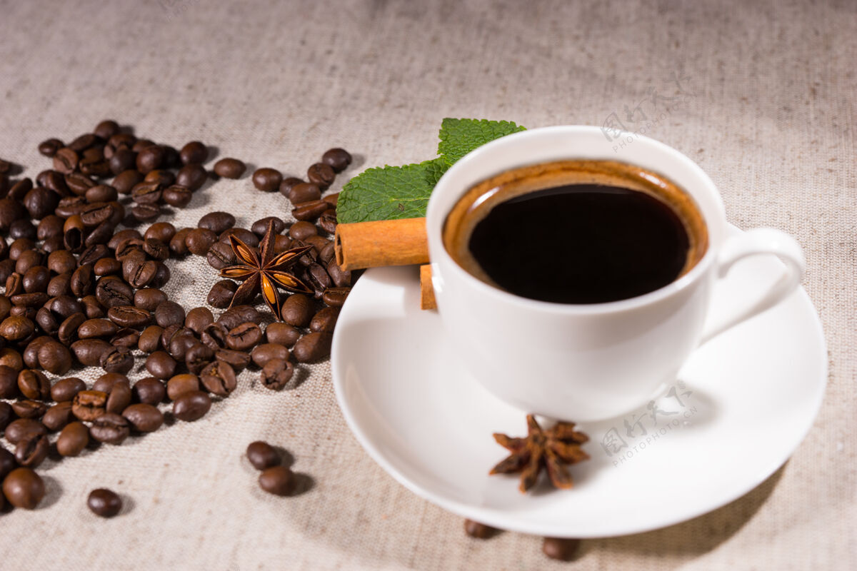 服务新鲜的黑咖啡在马克杯里放在白色盘子里 八角茴香和松豆子放在自然色调的画布上桌布咖啡屋休息