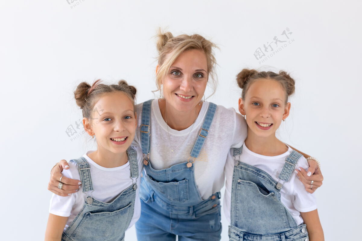 女性家庭 姐妹和爱的概念-母亲拥抱两个双胞胎女儿在白色的表面表情乐队快乐