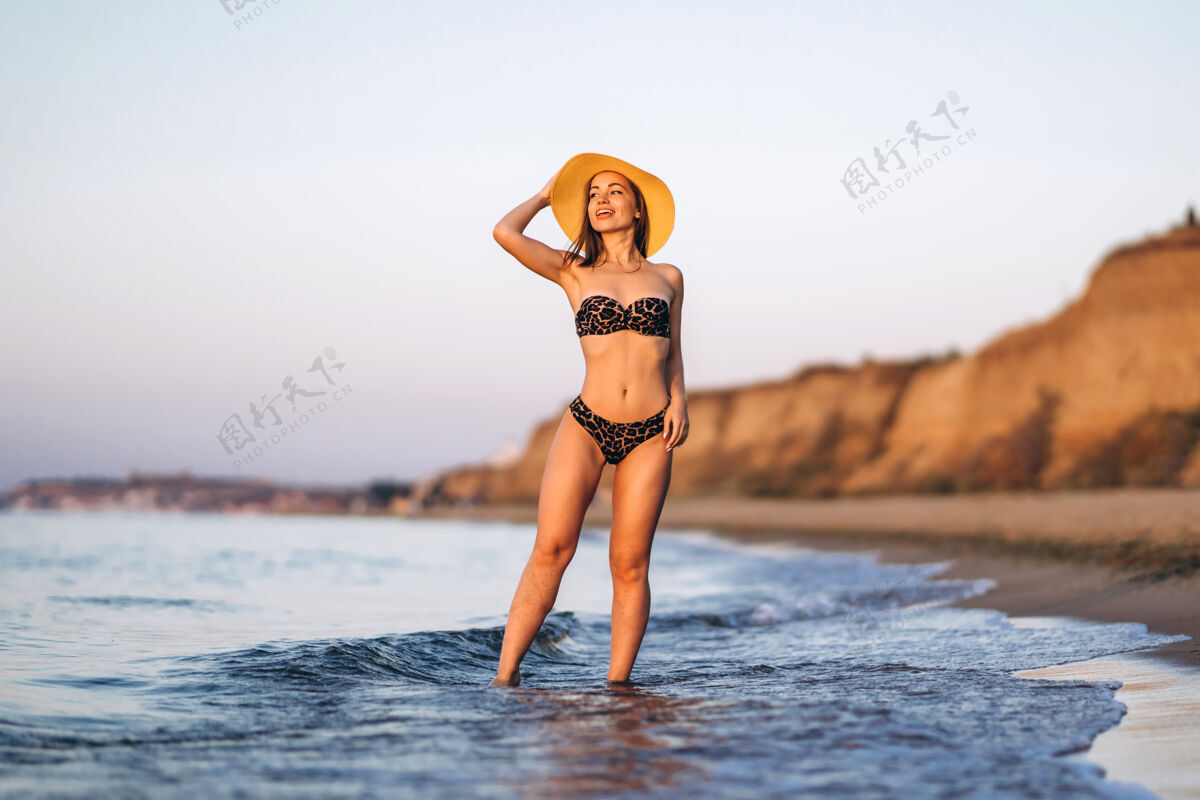 女人漂亮的黑发女人在海边的海滩上放松漂亮帽子户外