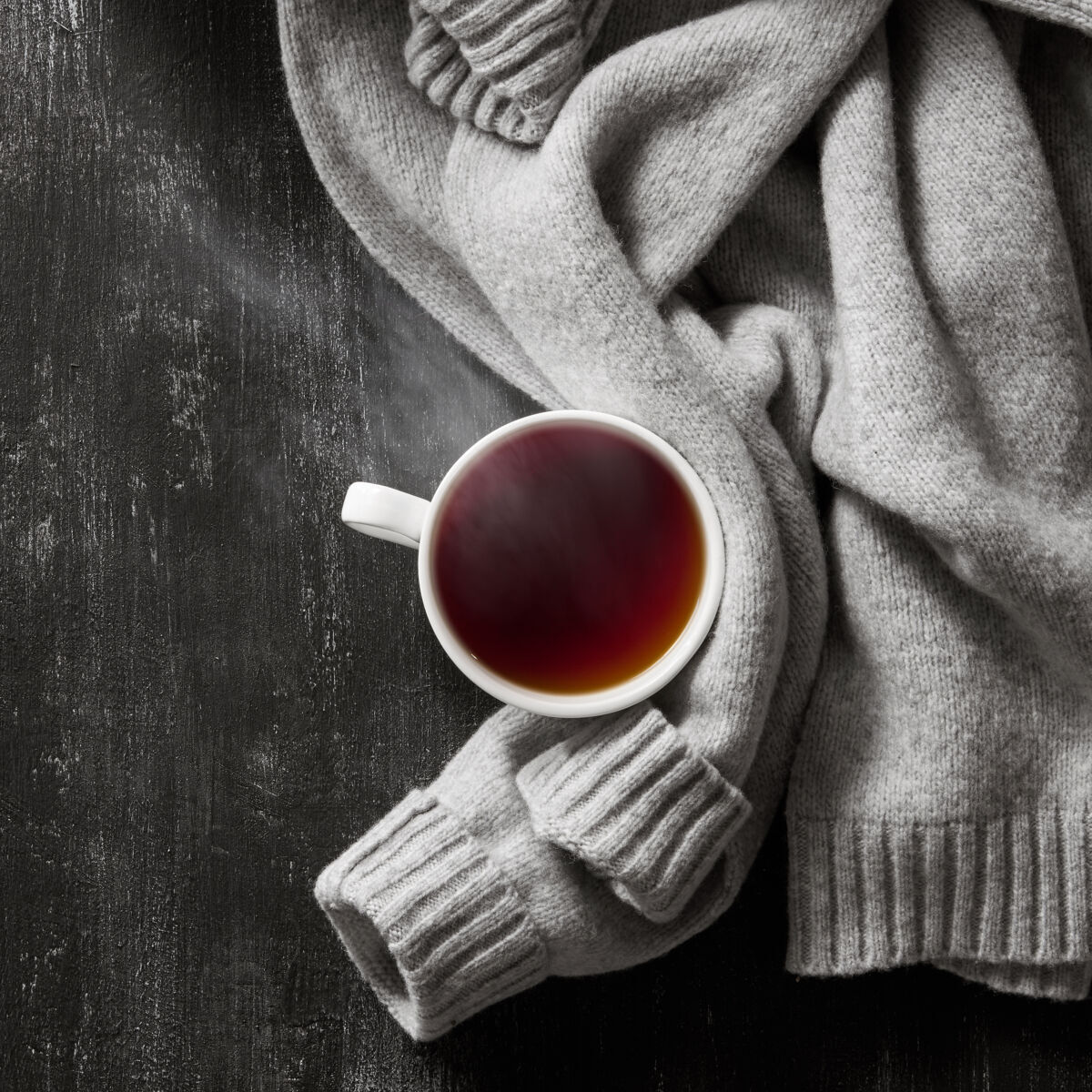 编织灰色舒适的针织毛衣与一杯茶在木制的黑色桌子上茶衣柜温暖