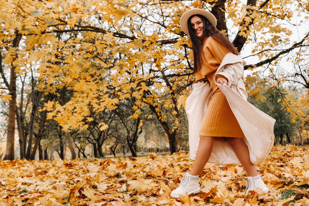 太阳一个穿着白大衣戴着白帽子的快乐女孩在秋天微笑公园肖像一个微笑的女人在金色的秋天秋季公园帽子小