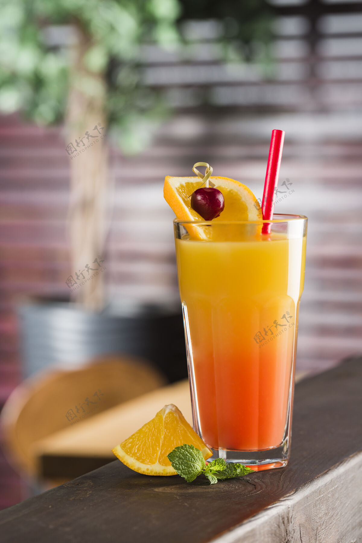 橙子热带鸡尾酒在一个高玻璃杯与一片橘子和薄荷在餐厅内部果汁吸管水果