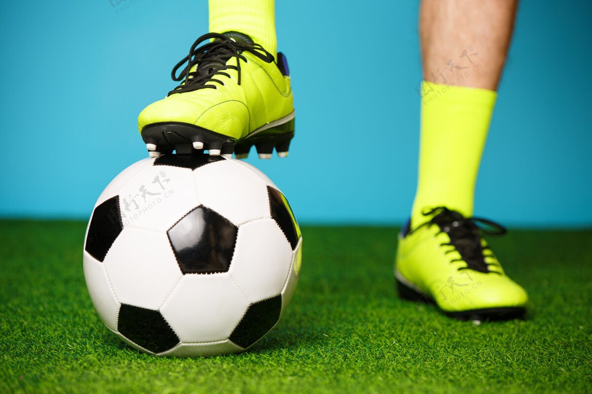 比赛在绿草和蓝色背景上拿球的足球运动员脚足球人类