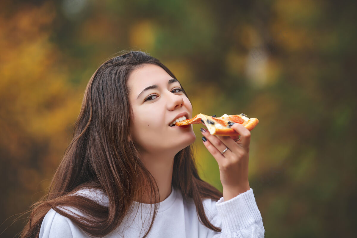 饮食年轻漂亮开朗的女孩一边吃比萨饼一边享受大自然的味道快餐最好零食