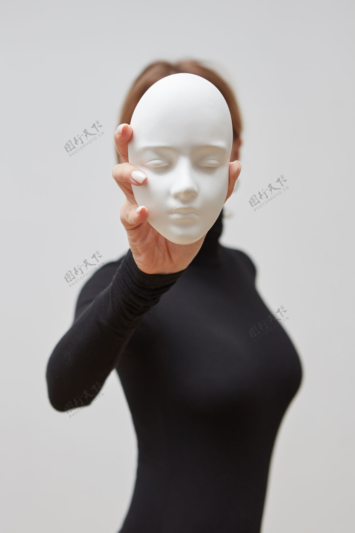 女性一个穿黑色套头衫的女孩在一堵白色的墙上举着石膏雕塑而不是脸文本.概念我们戴的面具面具双重瓷器