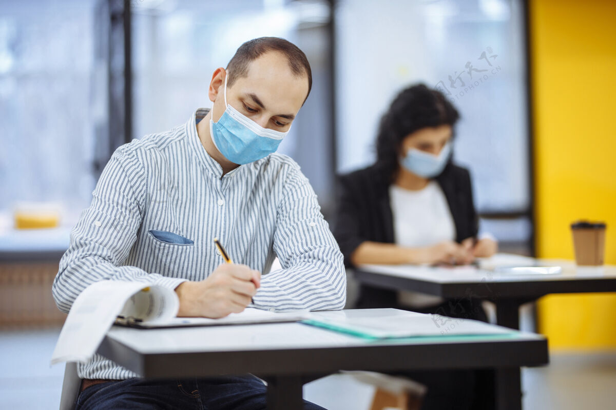 商业年轻的商人在一家医院的covid-19大流行期间努力工作办公室男专业人士戴着医用面罩坐在办公桌前 查看商业趋势文件流行病面具