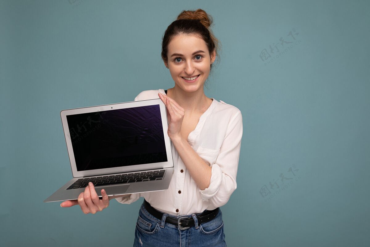 技术美丽微笑的年轻女子拿着上网本电脑看着相机穿着白色衬衫隔离在蓝色背景上游戏电脑笔记本电脑