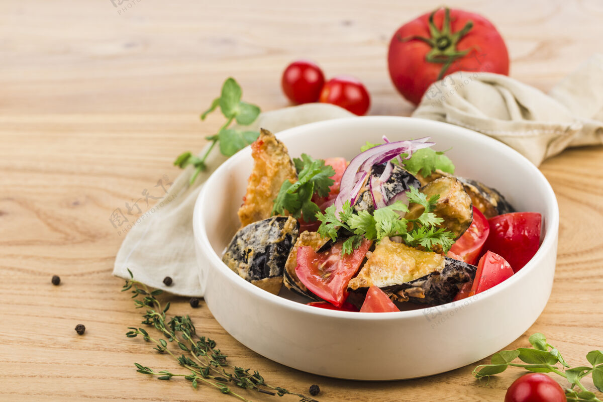 西红柿用烤茄子 西红柿 红洋葱和新鲜香草做成的沙拉 放在一个浅色的木制盘子里烘焙盘子木头