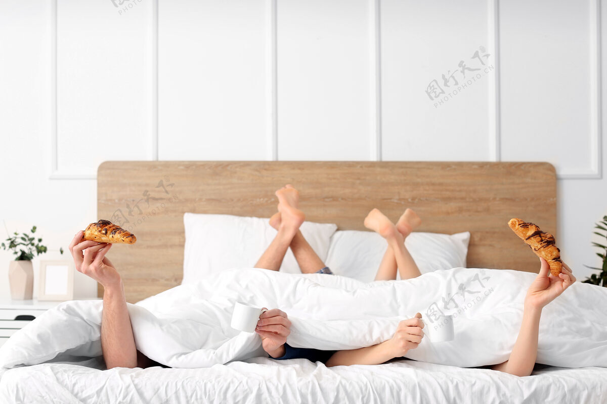 盖年轻夫妇在家里床上吃早餐一起休息毯子