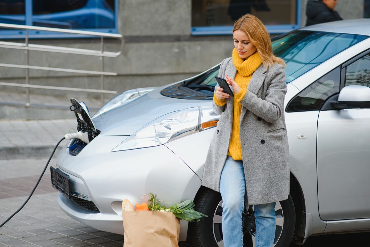 能源一个女人拿着电话靠近一个出租的电器汽车在充电站充电女性女孩交通