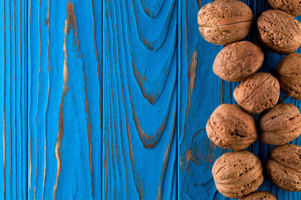 成熟整个胡桃树在漆成蓝色的木桌上的俯视图碗分散果壳