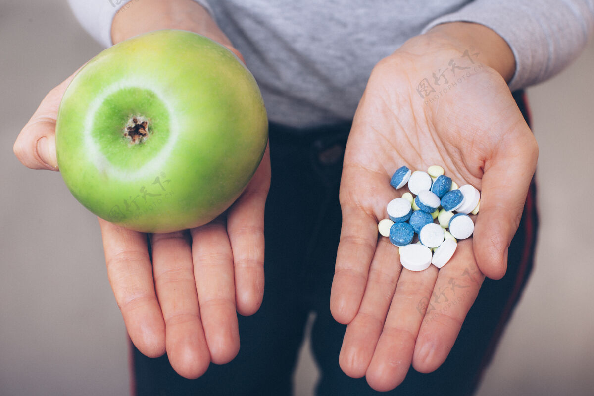 药物特写手的上视图 一只手拿着苹果 一只手拿着药丸另一个女人展示提高免疫力的方法 通过自然或药物的方式苹果吃食物