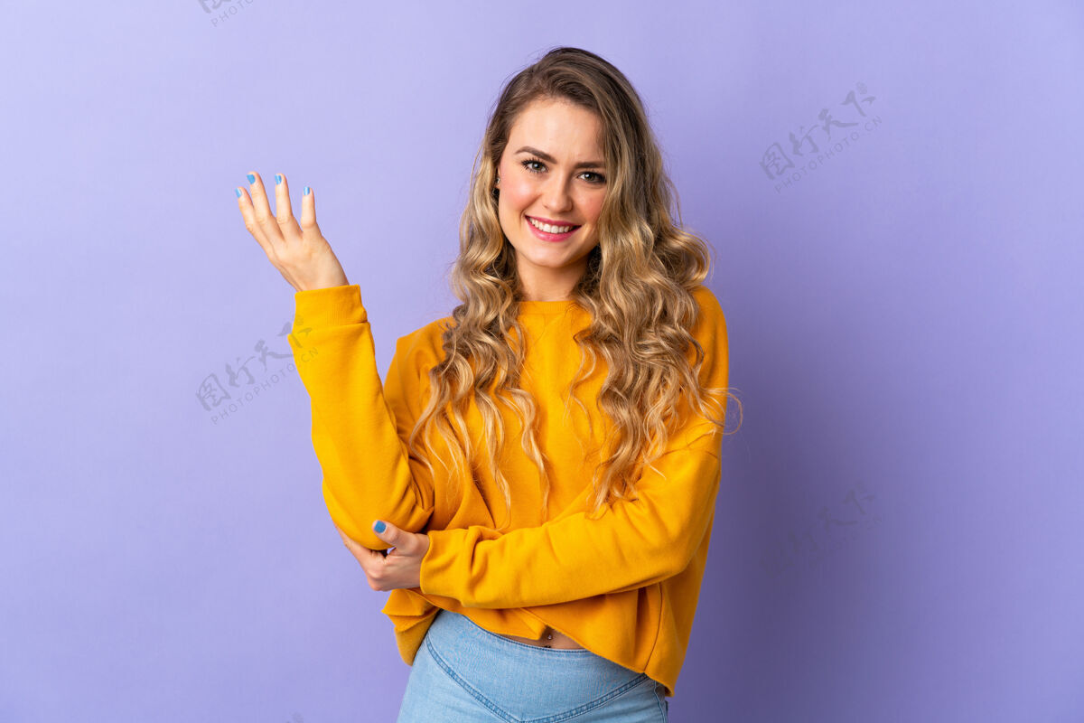 彩色一位被隔离在紫色背景上的巴西年轻女子向侧面伸出双手 邀请前来墙壁手女孩
