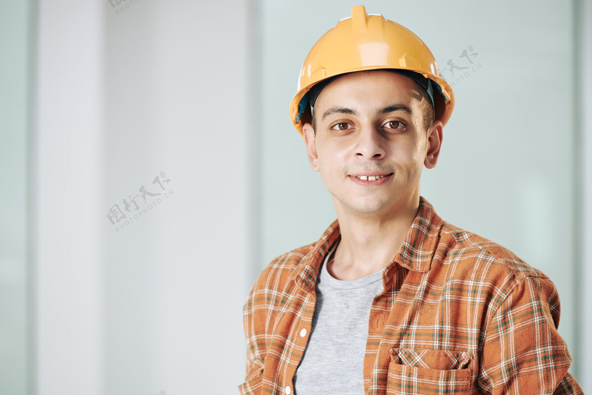 站立年轻的中东建筑工程师戴着安全帽微笑着看着镜头格子布成人男性