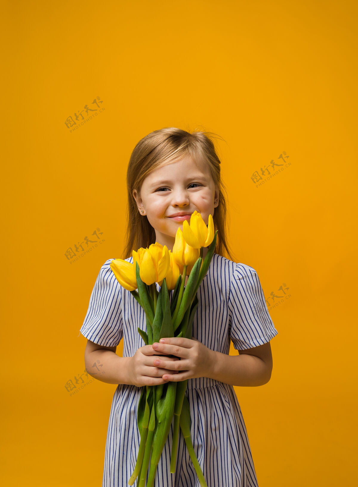女性一个微笑的小女孩的肖像 黄色的郁金香上有一束黄色的郁金香脸黄色礼服
