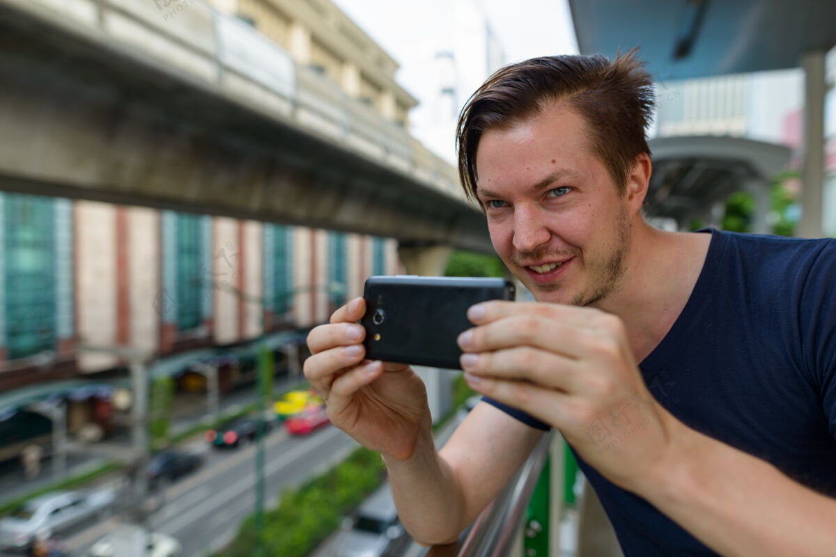 影响者在天空火车站用手机拍照的快乐年轻帅哥的脸斯堪的纳维亚交通拍摄
