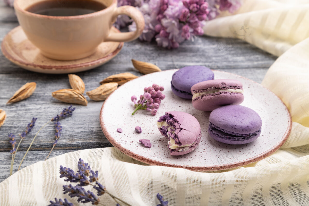 糕点紫色的马卡龙或马卡龙蛋糕 在灰色木质表面和白色亚麻织物上放一杯咖啡面包房薰衣草杏仁饼