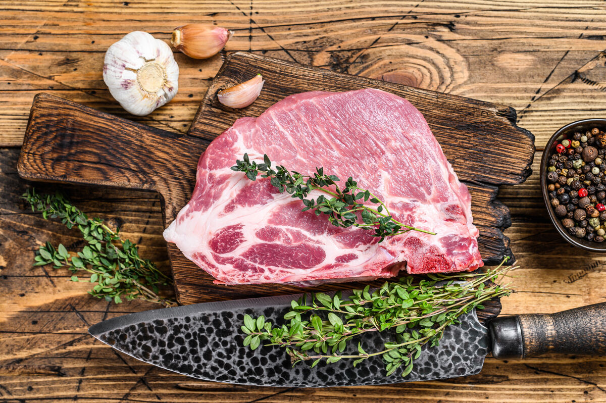 顶视图用刀在砧板上切新鲜的大理石肉排猪肉脖子迷迭香