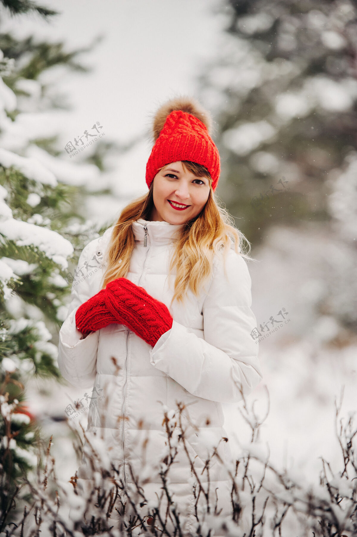 肖像一个穿着白衣服 戴着红帽子的女人在寒冷的冬天的肖像森林女孩在冰雪覆盖的冬季森林里新年女孩圣诞