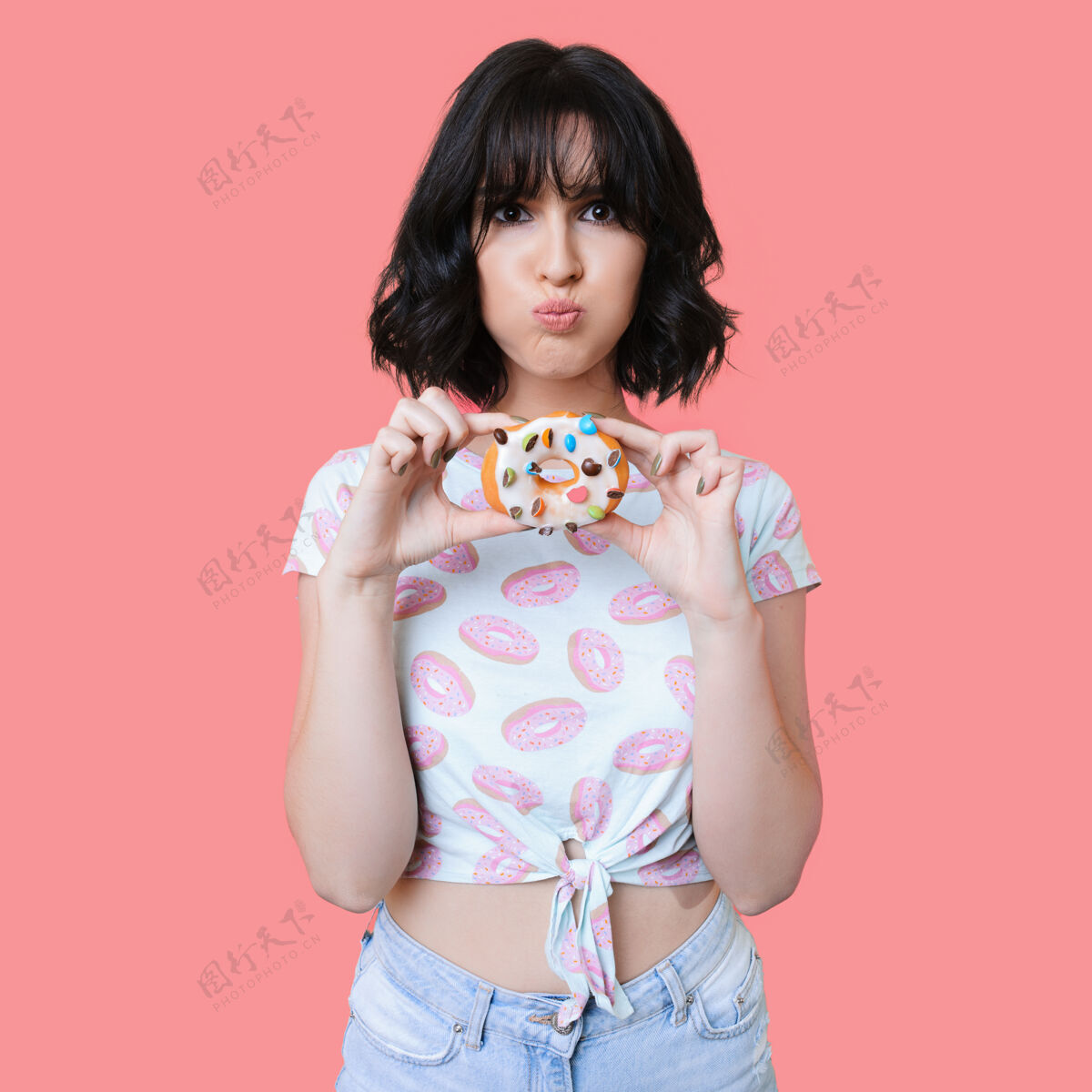 甜点迷人的黑发女士穿着时髦的衣服拿着美味的彩色甜甜圈 在粉红色的墙上摆姿势年轻饮食情绪