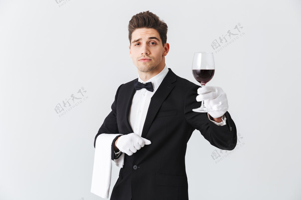 人年轻帅气的侍者穿着燕尾服 端着一杯红酒隔着灰色的墙管家举行酒