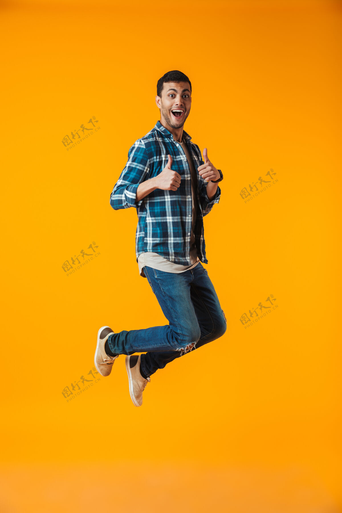 手一个穿着格子衬衫的快乐的年轻人的全长肖像被隔离在橙色的墙上 跳跃庆祝成功充分男酷