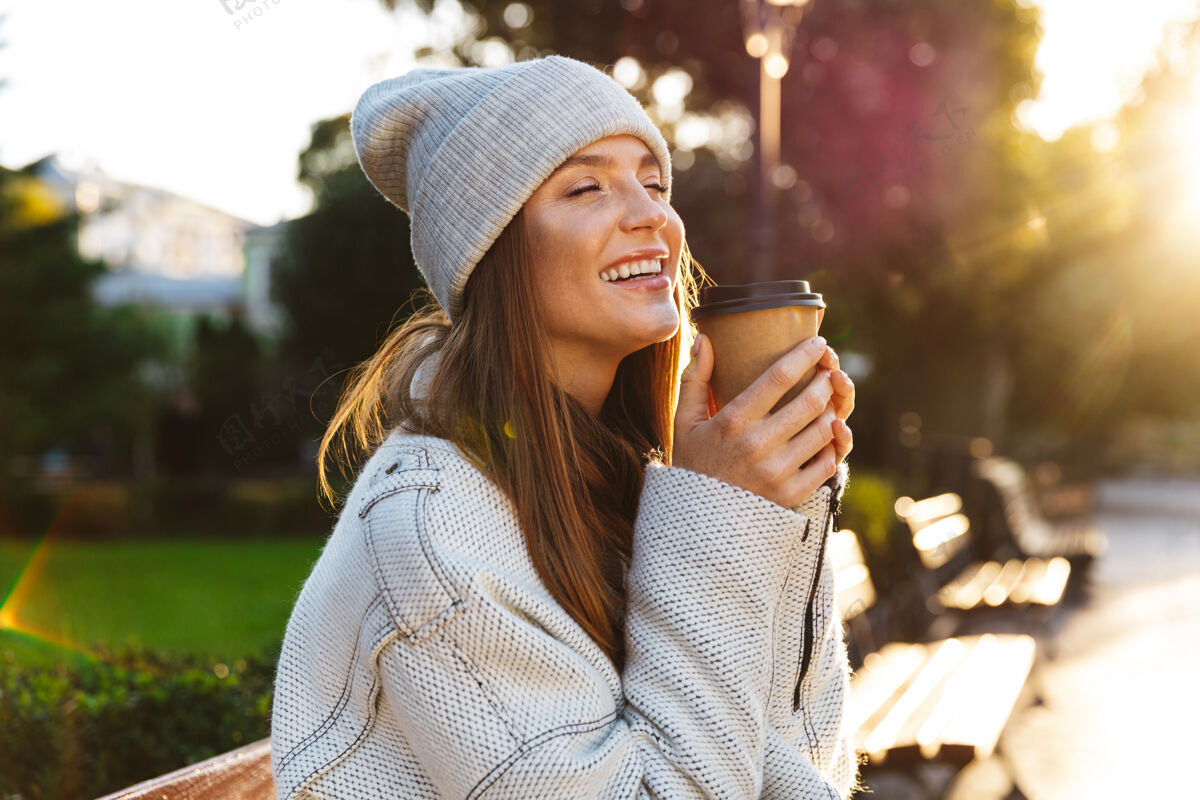 高加索美丽的年轻女子穿着秋大衣 戴着秋帽 坐在户外的长凳上 端着一杯热咖啡外套秋天魅力