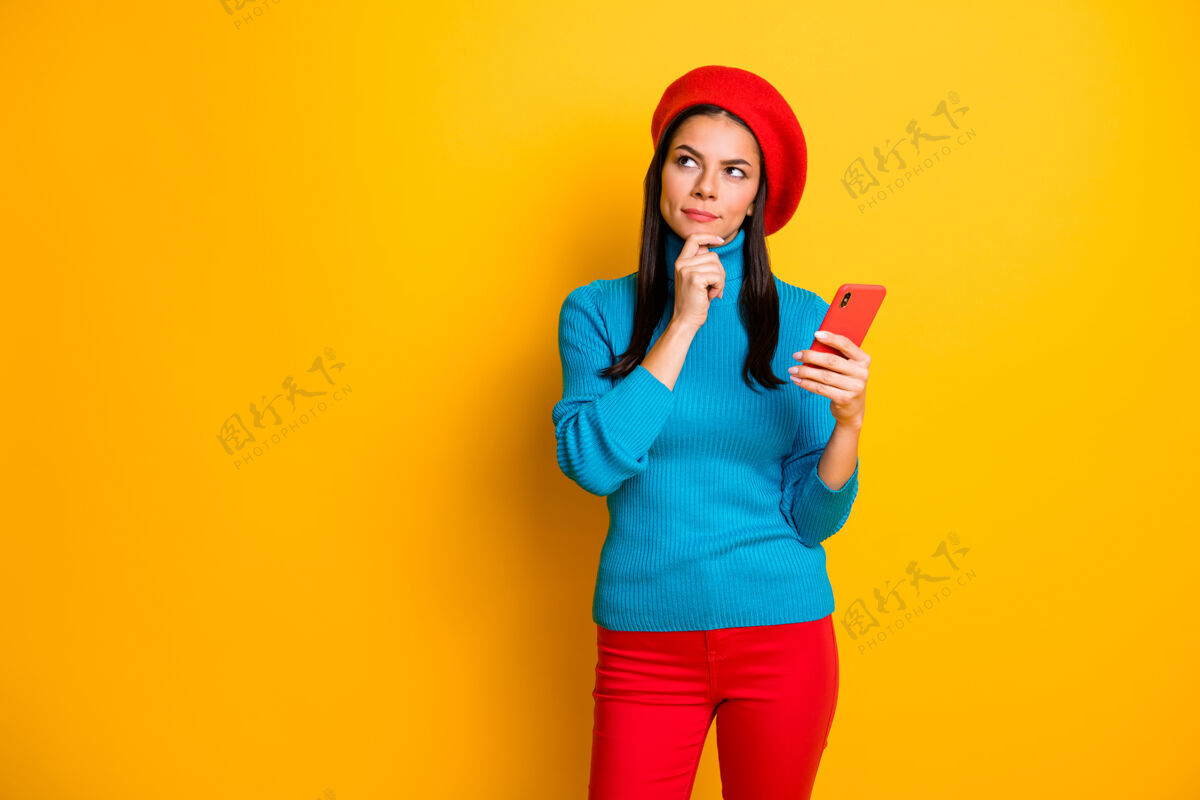 博客漂亮迷人可爱沉思认真认真的女孩做决定的肖像手拿着手机现代公共岗位smm隔离在明亮明亮明亮明亮的黄色墙壁上沉思毛衣聪明