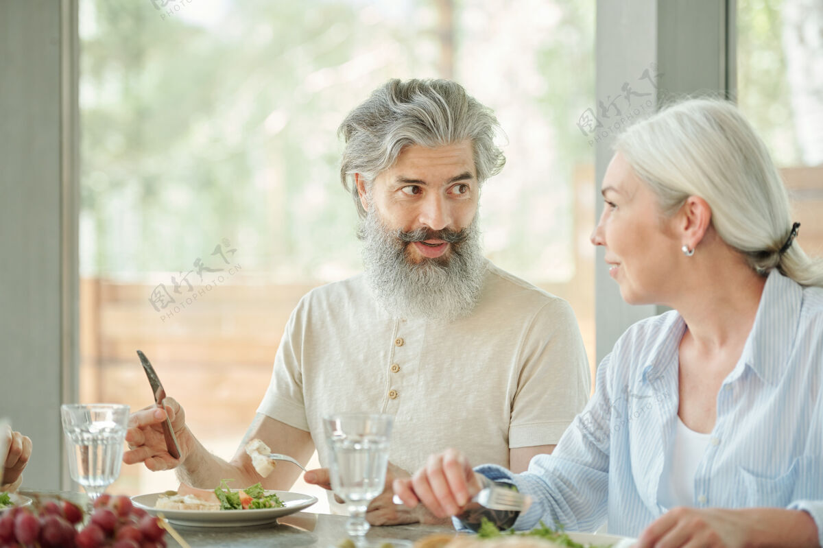 放松无法辨认的男人坐在桌子旁 用刀叉吃着清爽的沙拉白种人吃饭午餐